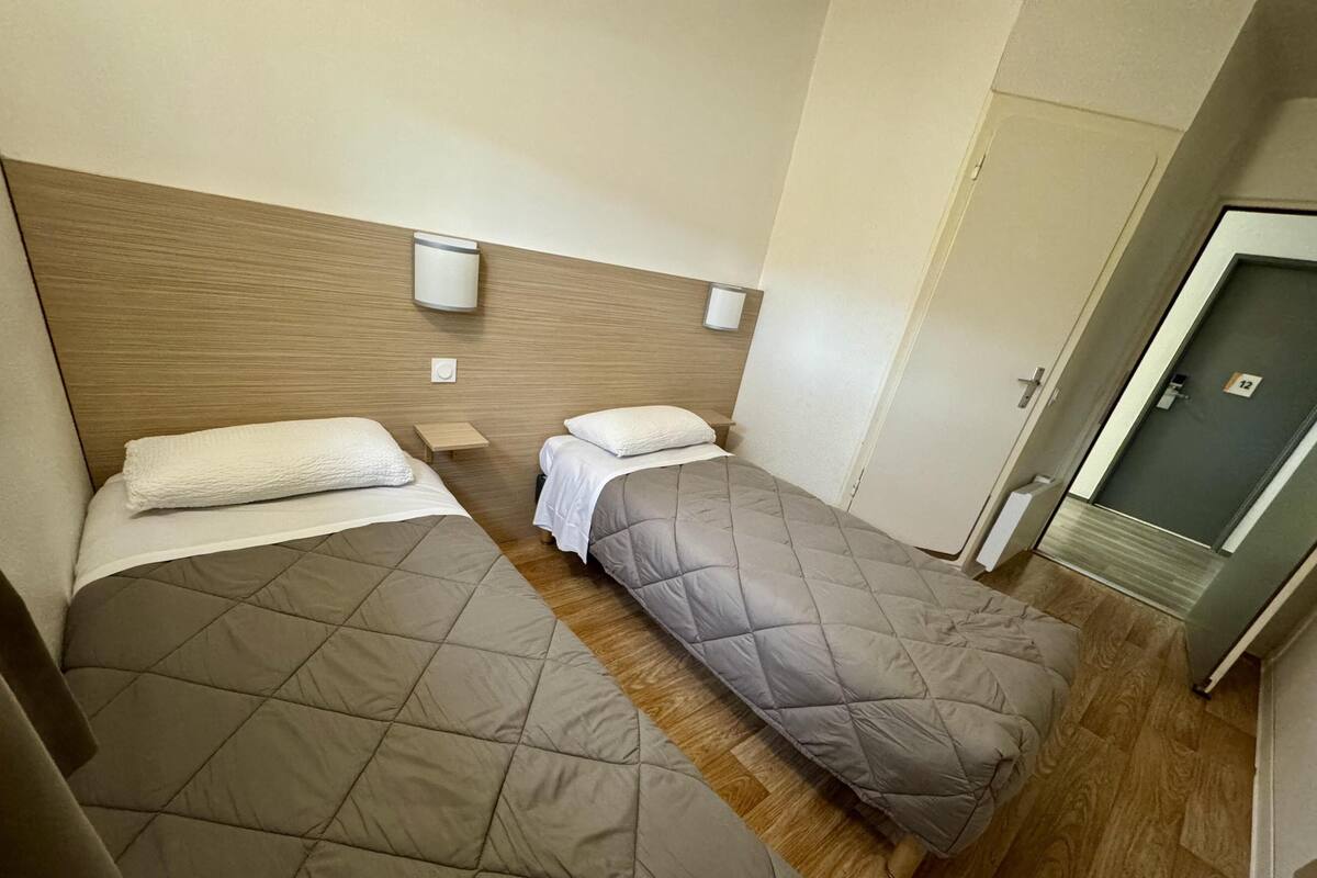 A hotel room with two beds, wooden headboard, bedside tables, and a door with a number.