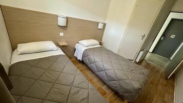 Une chambre d’hôtel avec deux lits, une tête de lit en bois, des tables de chevet et une porte portant un numéro.