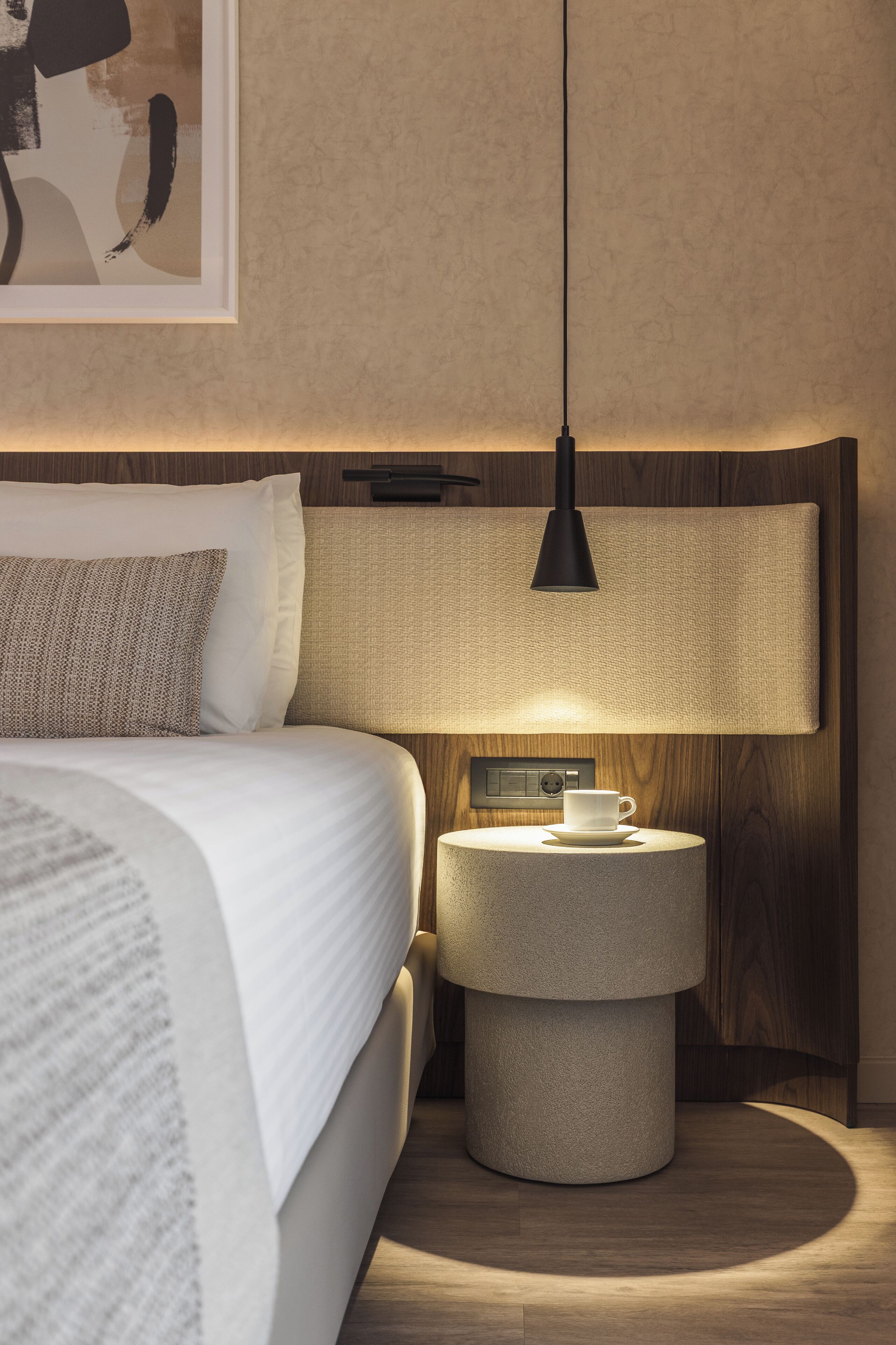 A neatly arranged bedroom with a bed, bedside table, lamp, and a wall-mounted control panel.