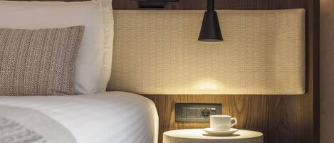 A neatly arranged bedroom with a bed, bedside table, lamp, and a wall-mounted control panel.
