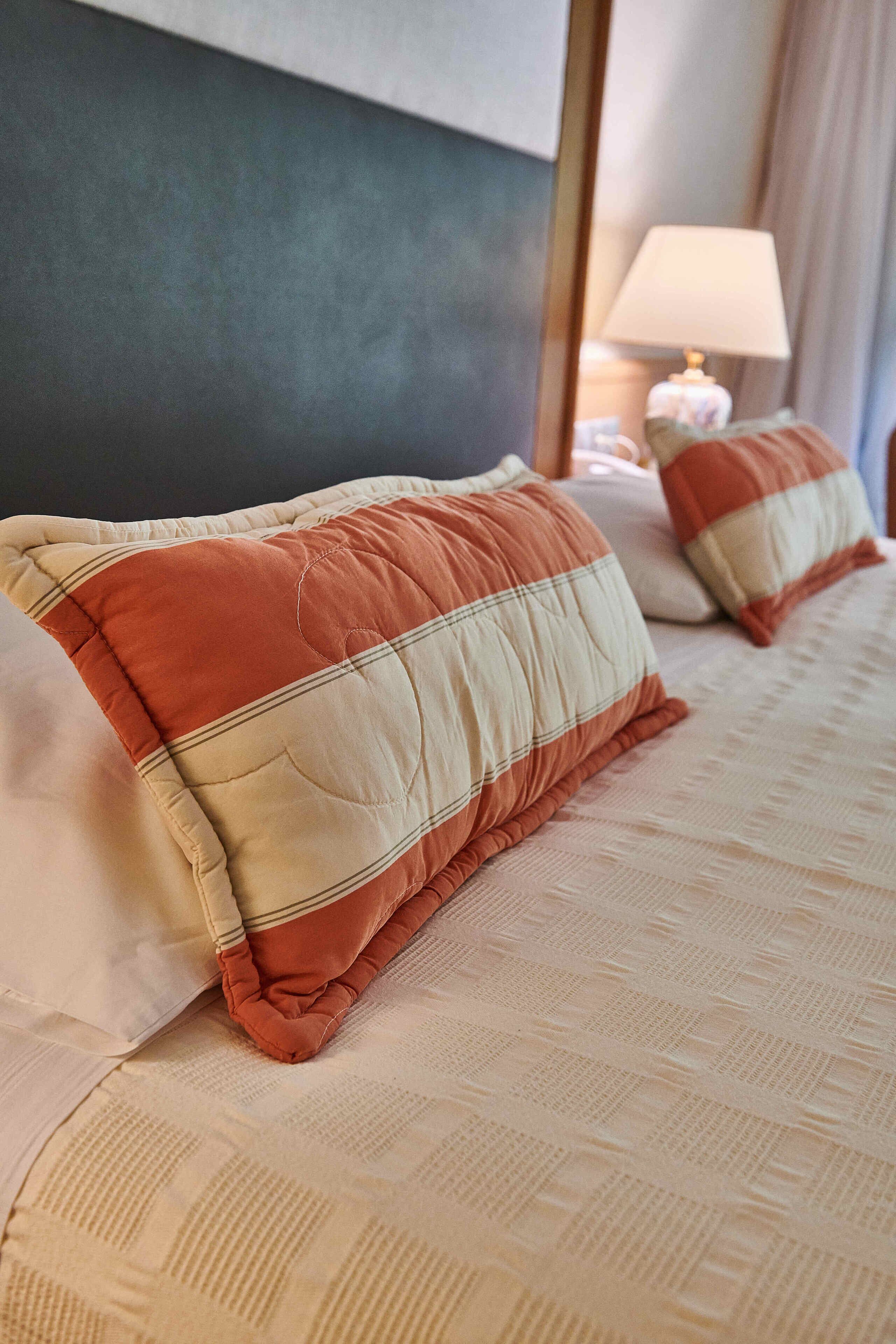 A bed with two pillows, a bedside table with a lamp, and a dark-colored headboard.