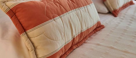Una cama con dos almohadas, una mesita de noche con lámpara y un cabecero oscuro.