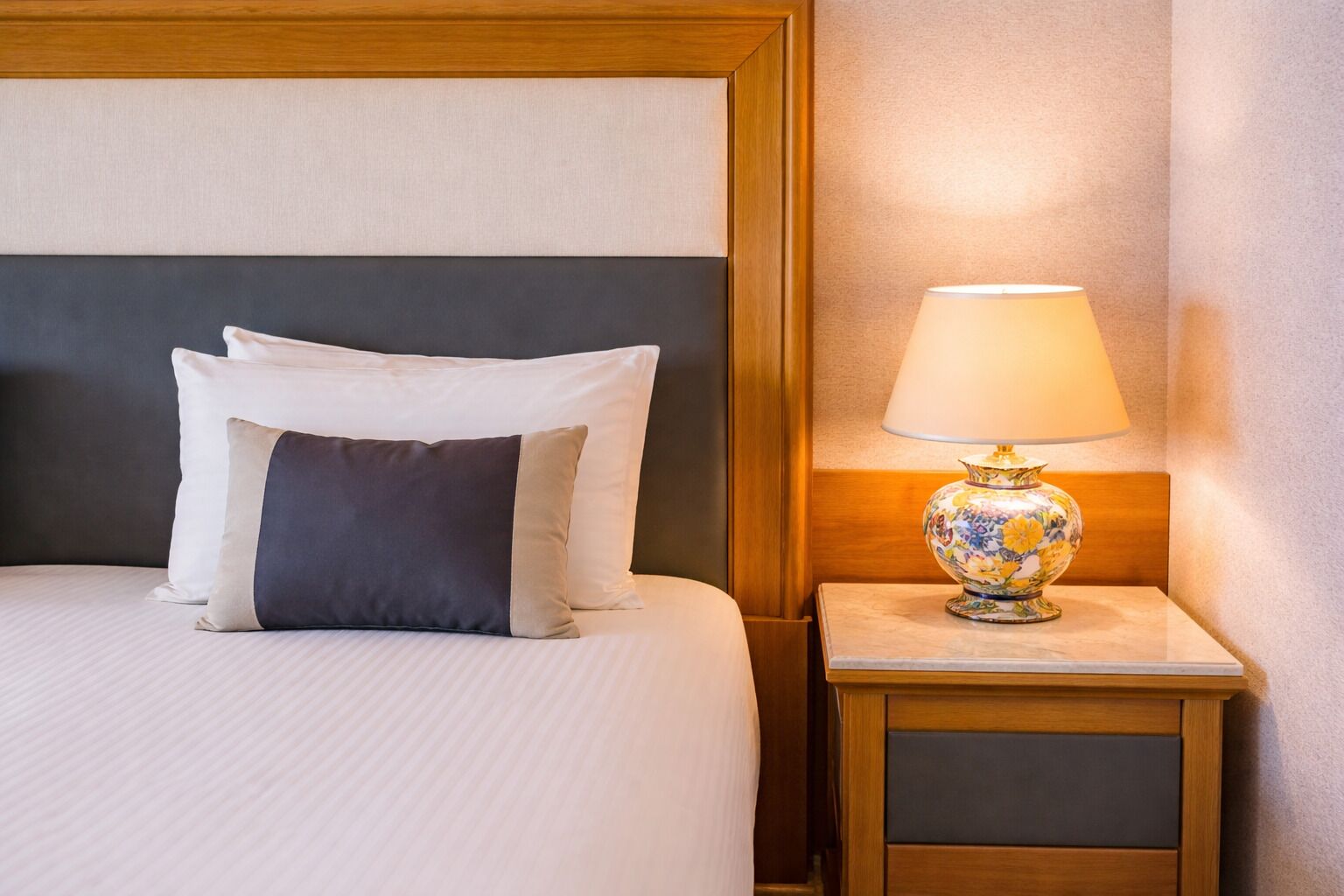 A neatly made bed with pillows, a bedside table with a lamp, and a wooden headboard.