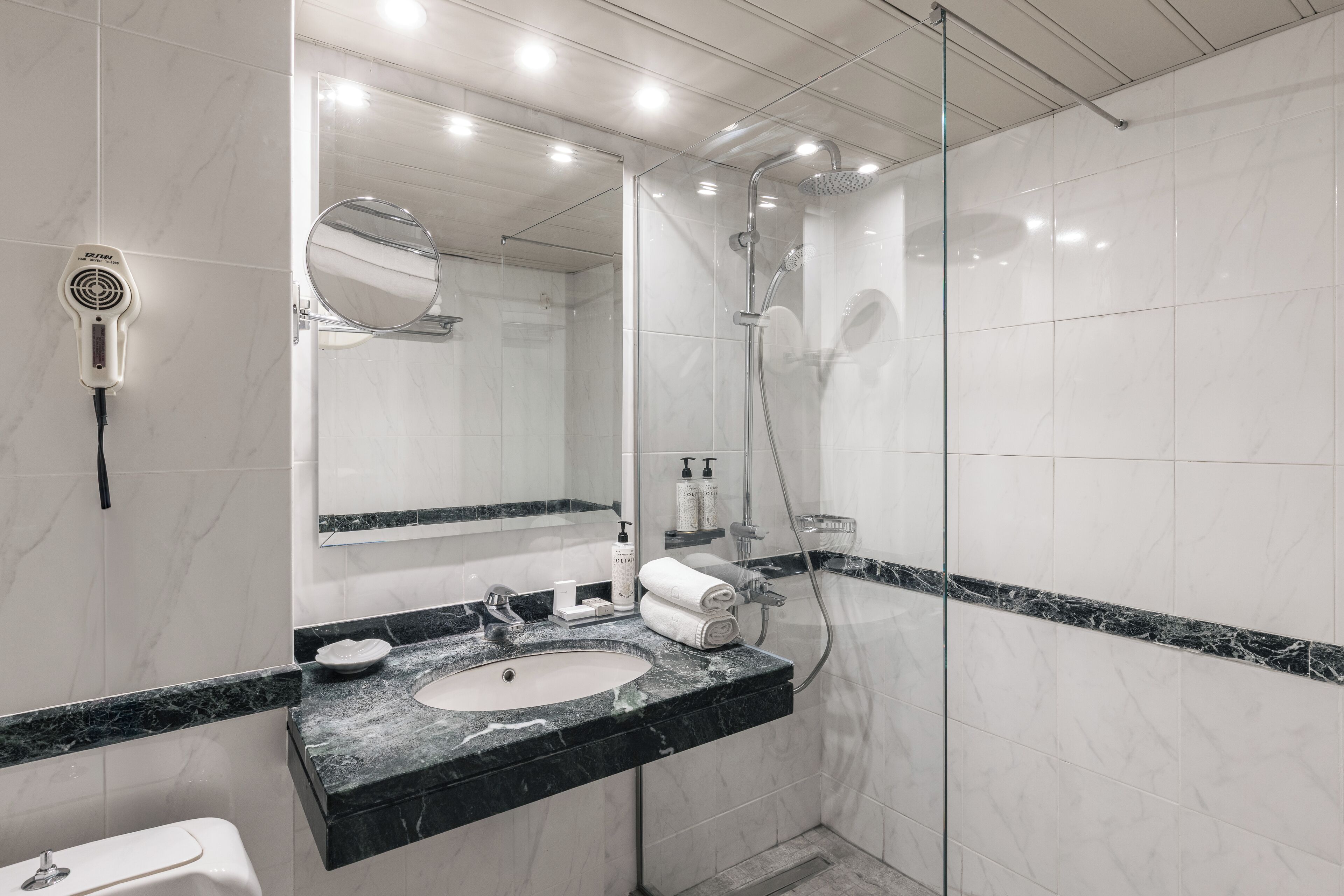 Een moderne badkamer met een marmeren wastafel, een douche met glazen wanden en een wandbevestigde haardroger.