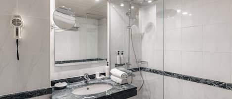 A modern bathroom with a marble sink, a glass-enclosed shower, and a handheld hair dryer mounted on the wall.