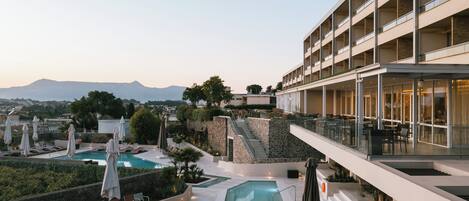A modern hotel with a rooftop pool, outdoor seating, and a view of mountains.