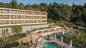 A hotel with multiple floors, outdoor pool area, and lush greenery in the background. - Divani Corfu Palace (Corfu)