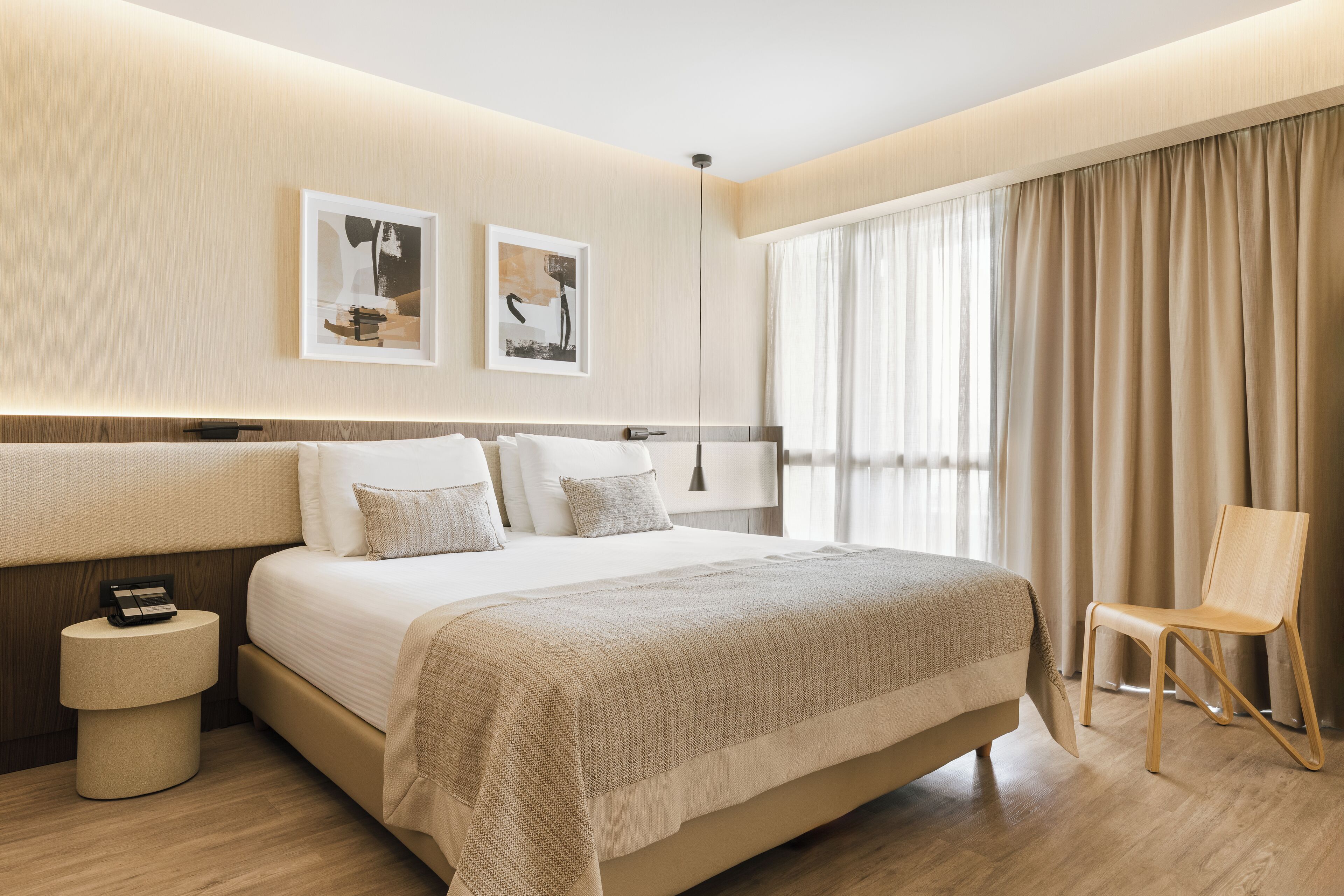 A modern hotel room with a large bed, bedside tables, a chair, and artwork on the wall.