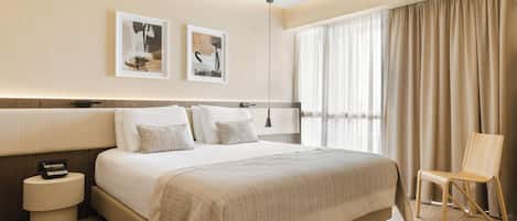 A modern hotel room with a large bed, bedside tables, a chair, and artwork on the wall.