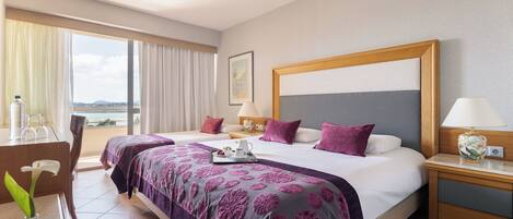Habitación de hotel con dos camas, un escritorio, una silla y vista al mar.