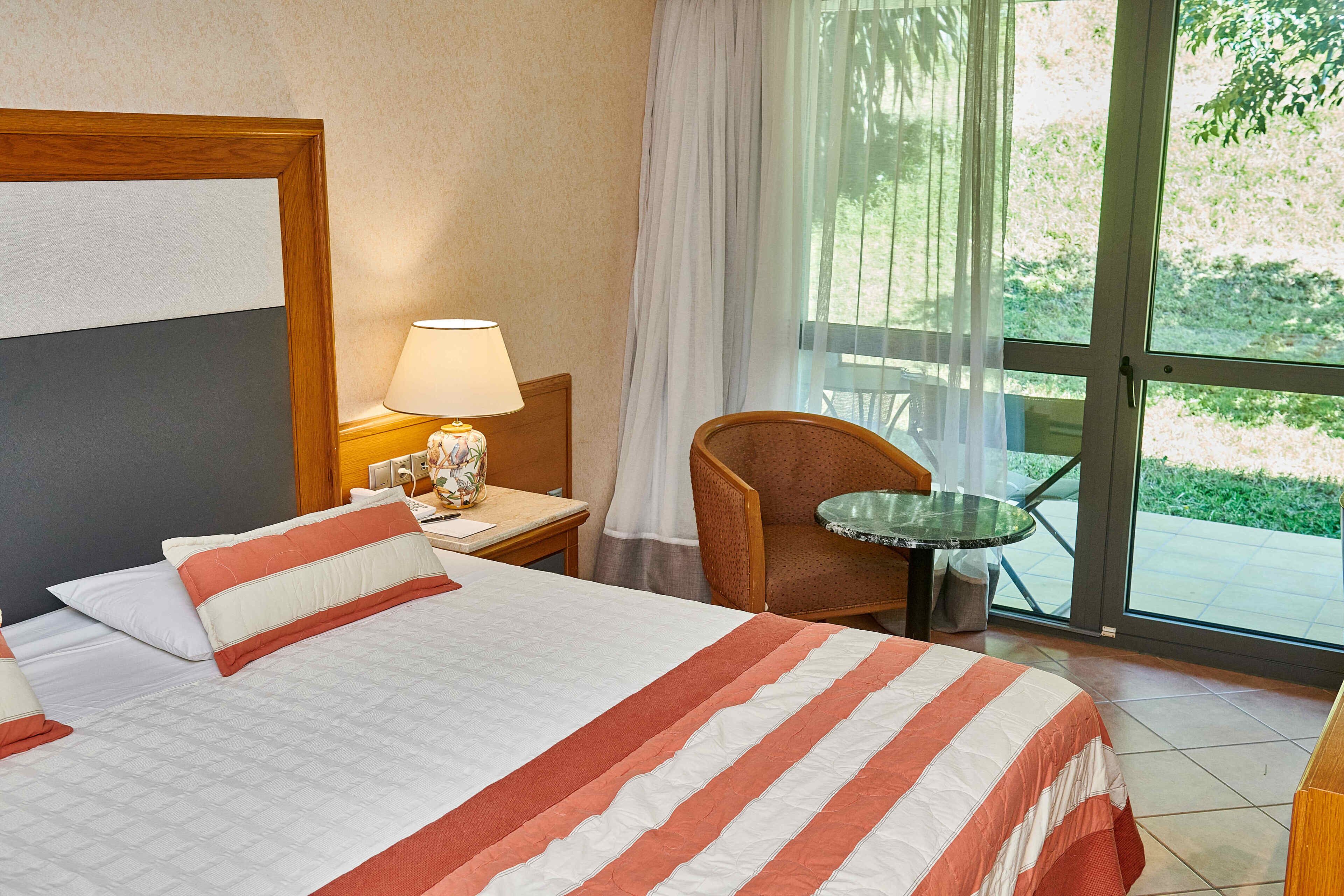 A hotel room with a bed, a nightstand, a lamp, a chair, and a table.