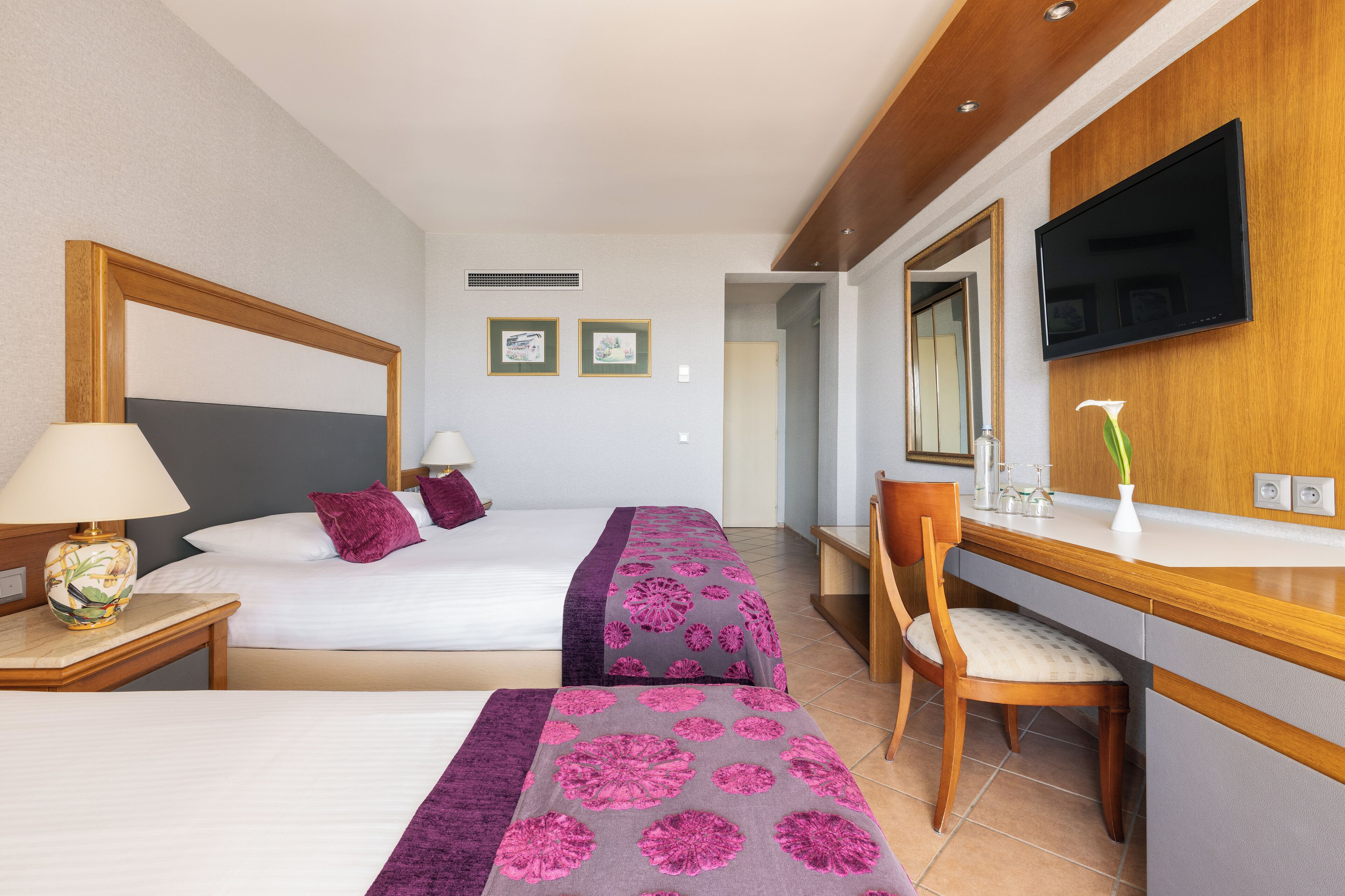 A hotel room with two beds, a desk, a chair, a TV, and a mirror.