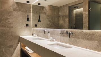 A modern bathroom with two sinks, a wooden bench, and pendant lights.
