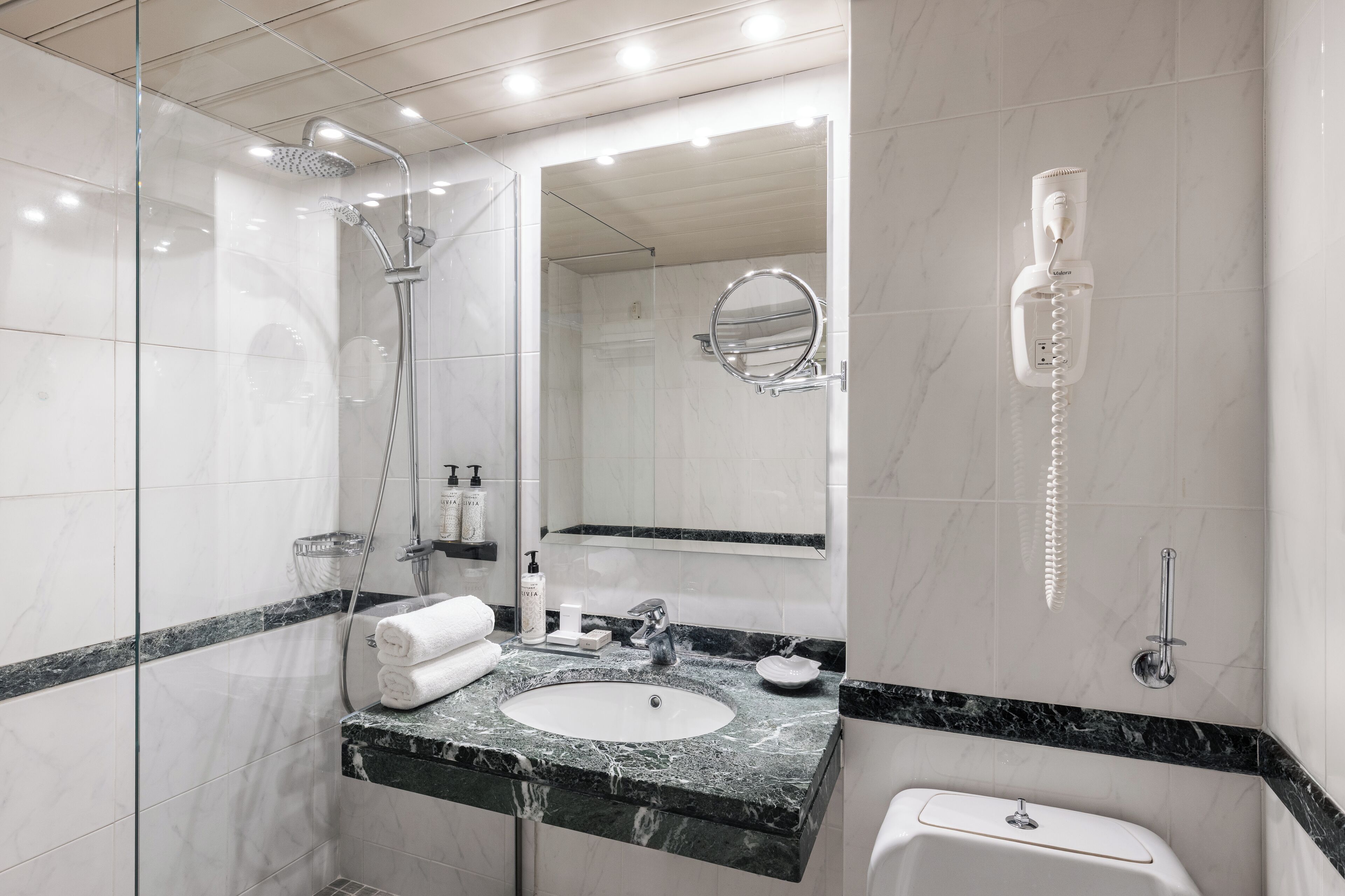 A modern bathroom with a glass-enclosed shower, a sink with a marble countertop, a toilet, and a mirror with a built-in light.