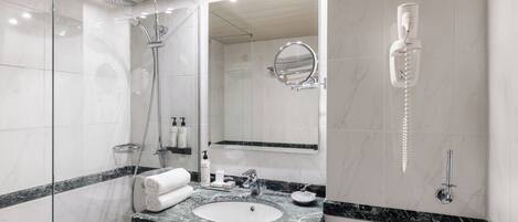 A modern bathroom with a glass-enclosed shower, a sink with a marble countertop, a toilet, and a mirror with a built-in light.
