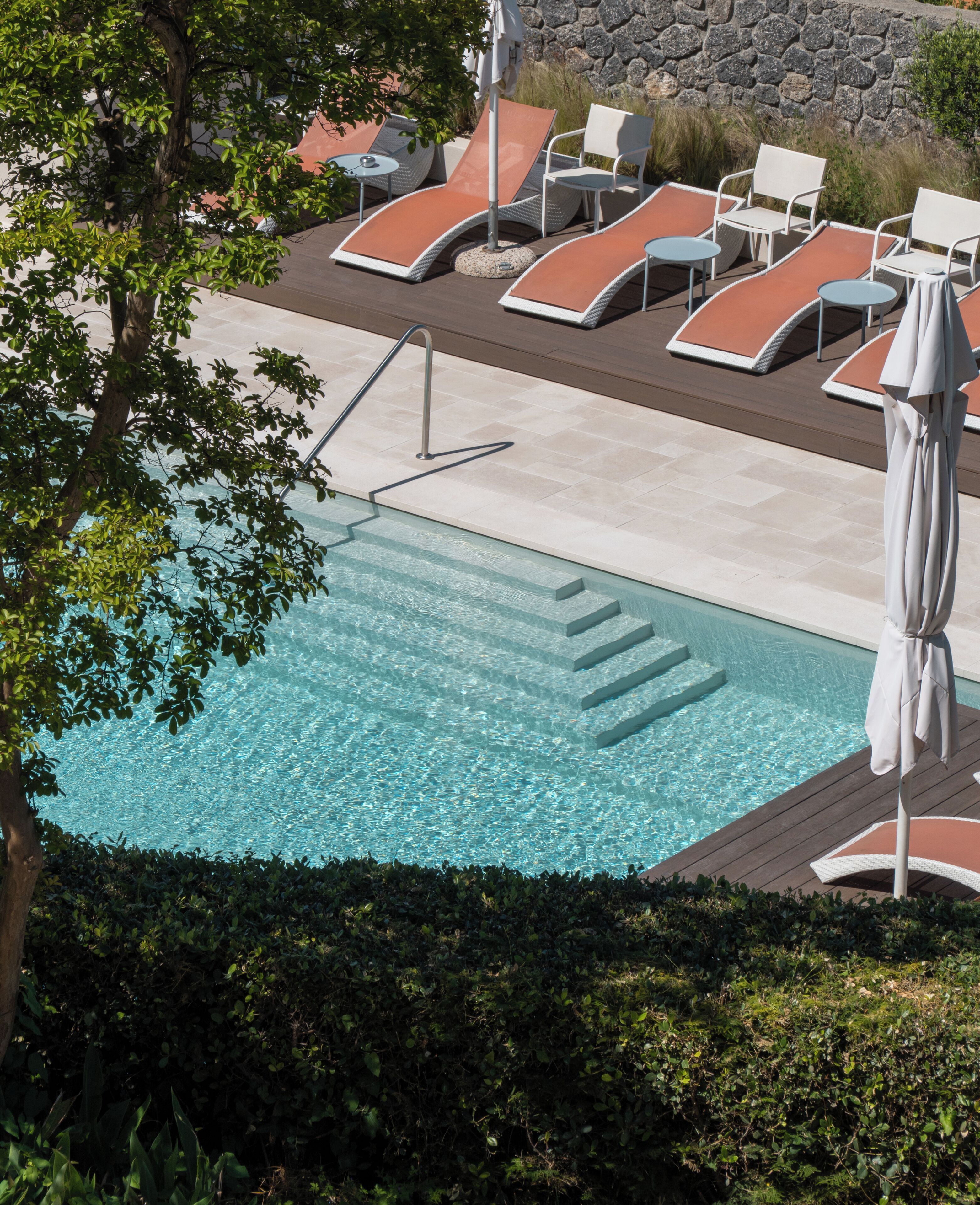 Ein Schwimmbecken mit Liegestühlen und einer Steinmauer im Hintergrund.