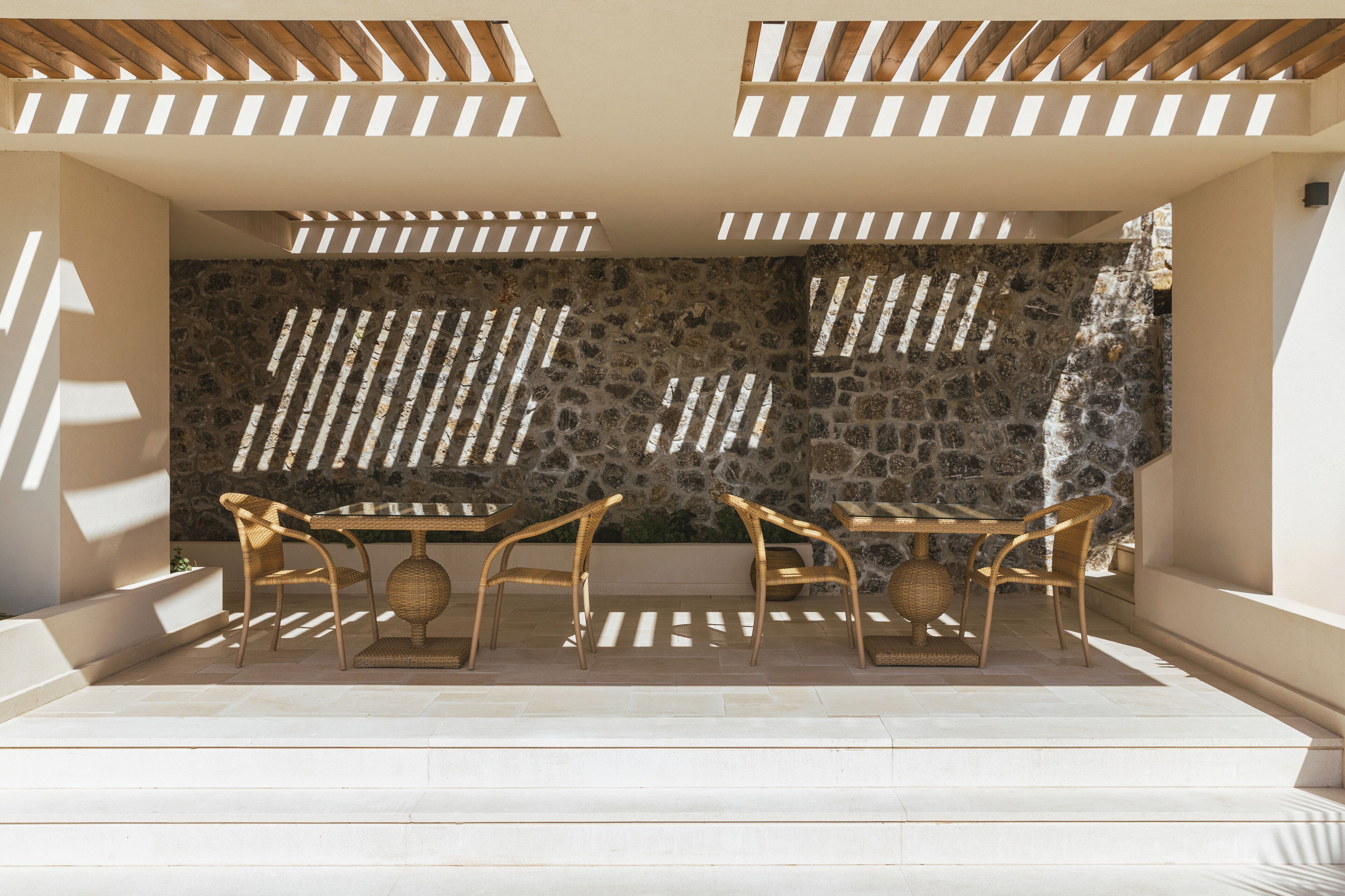 An outdoor seating area with stone walls, wooden slats, and wicker furniture.