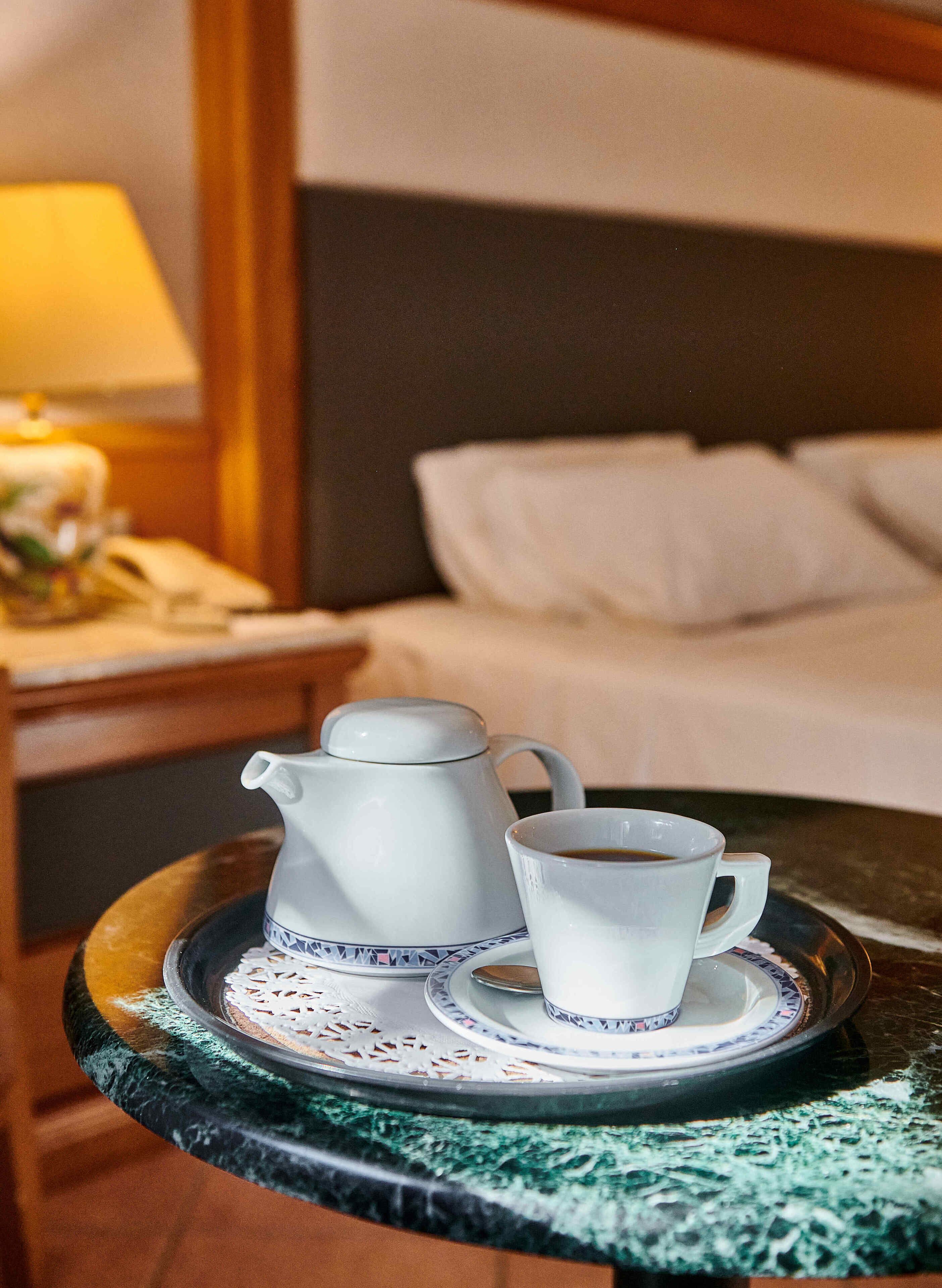 A tray with a teapot and a cup on a table in a hotel room.