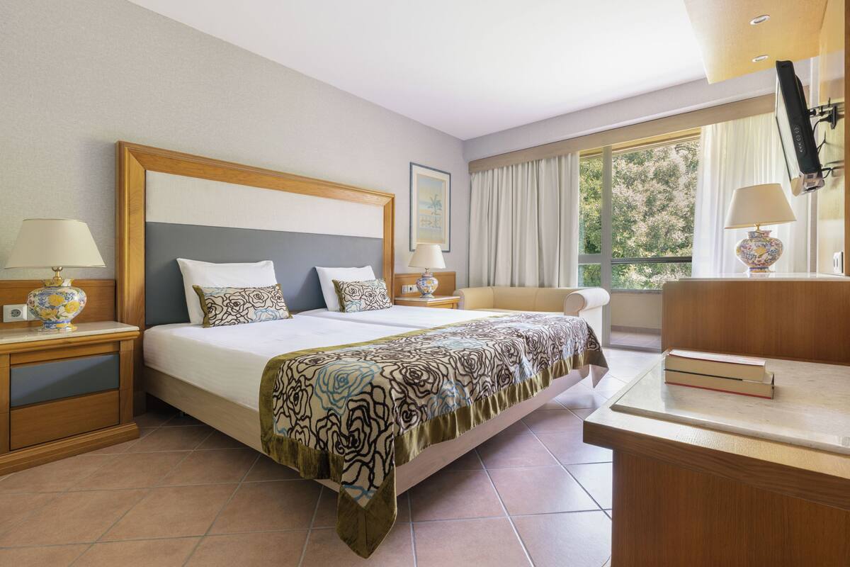 A hotel room with a large bed, two bedside tables, a desk, and a window with curtains.