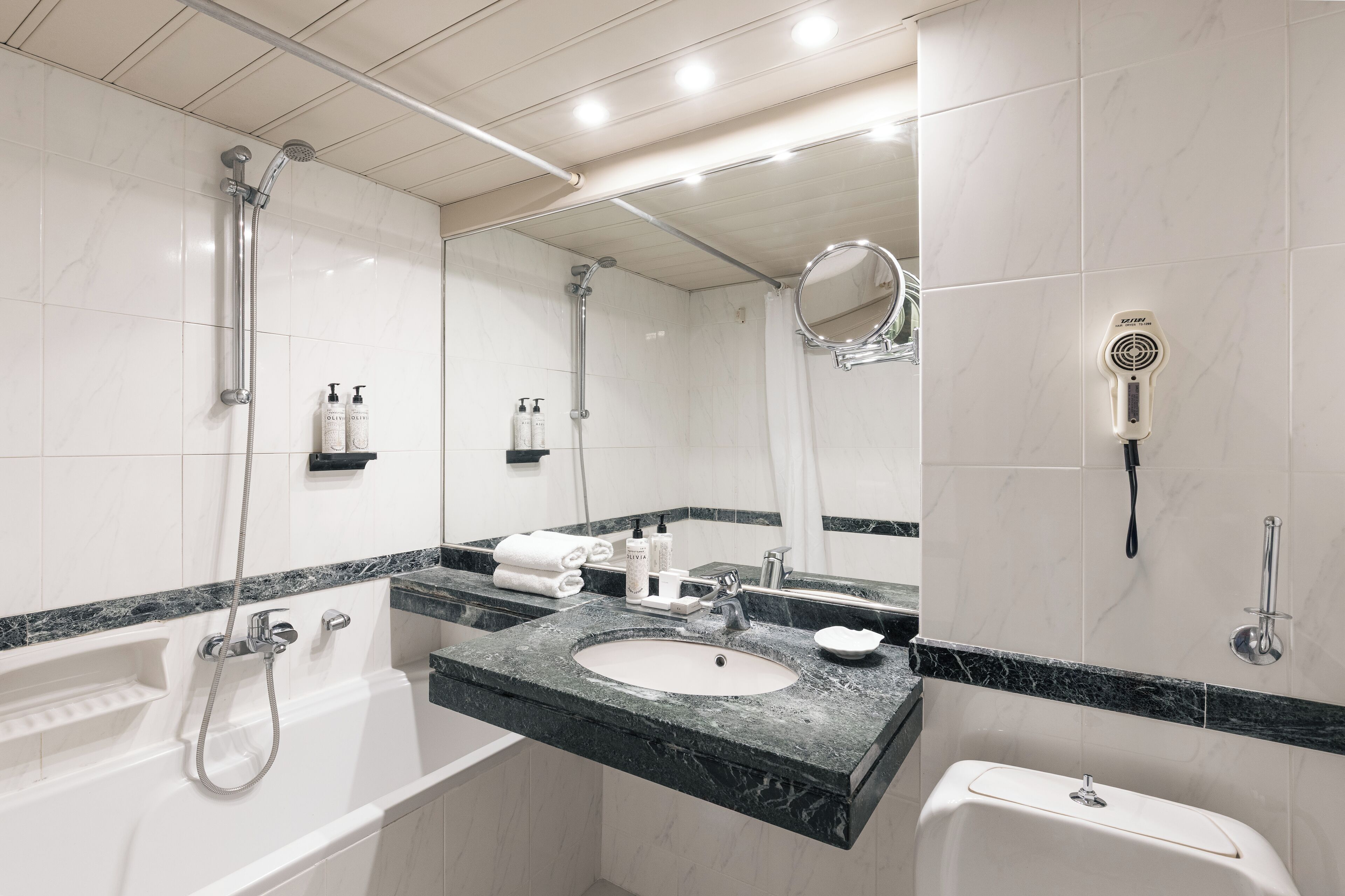 A modern bathroom with a white bathtub, a sink with a marble countertop, a mirror, and a handheld showerhead.