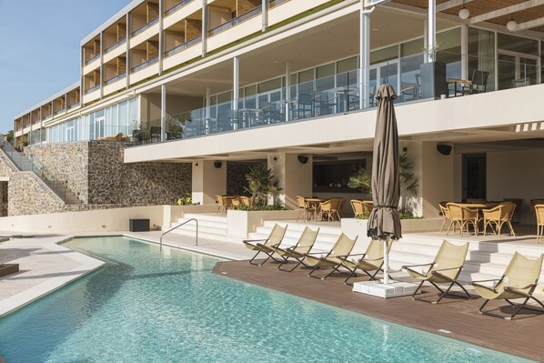 A pool area with lounge chairs and a staircase leading to a building with multiple balconies.