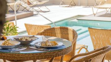Un espace extérieur avec une piscine, des meubles en osier et une table dressée pour les repas.
