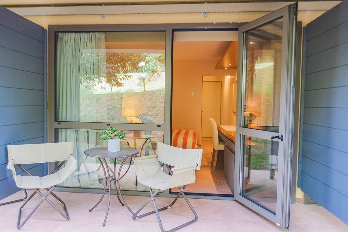 An open sliding glass door leading to a patio with two chairs, a small table, and a potted plant.