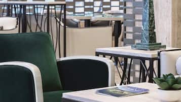 Interior de restaurante com cadeiras estofadas em verde, uma mesa de mármore e um pilar decorativo.