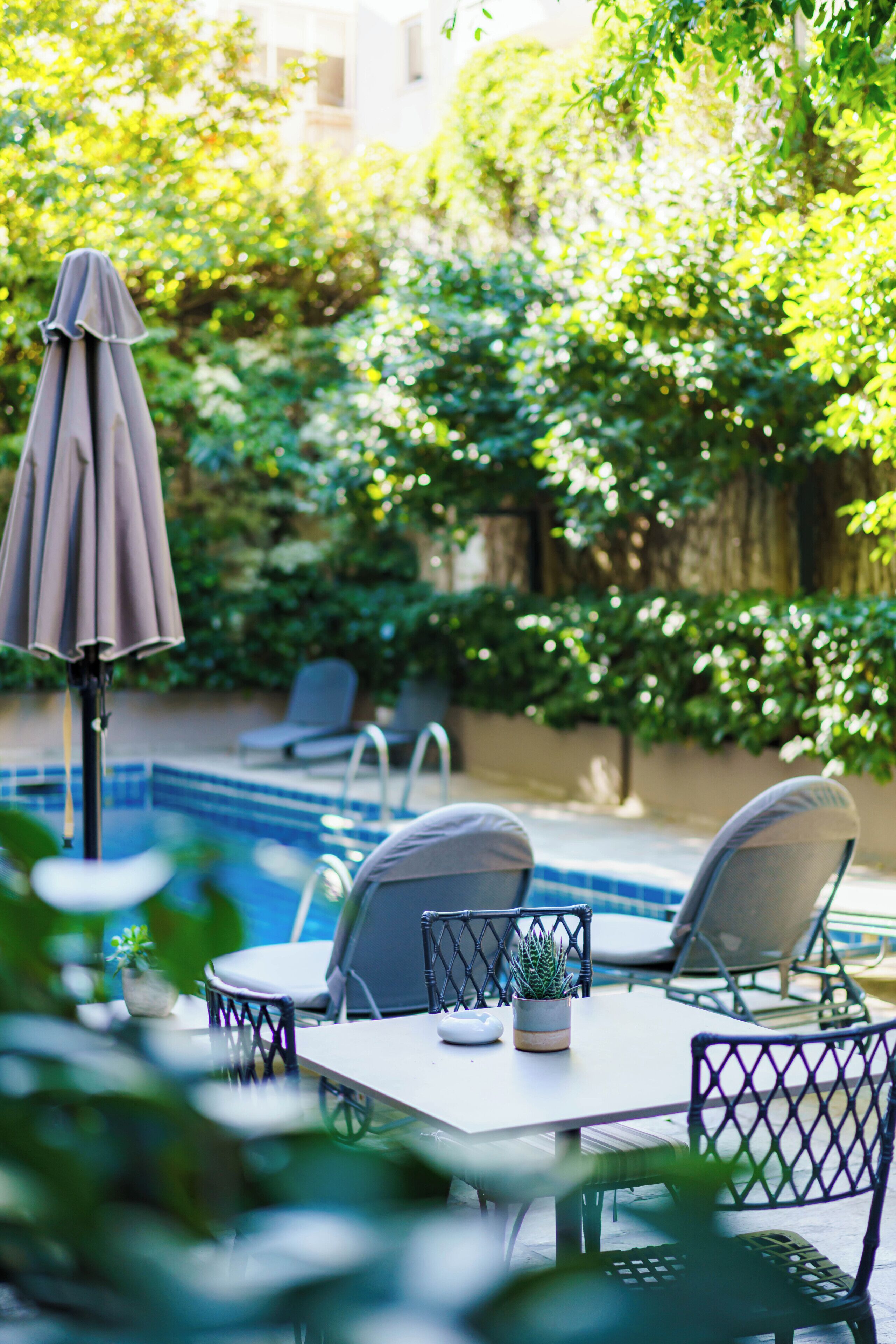 A poolside area with a table, chairs, and an umbrella.