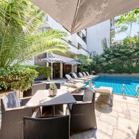 Área externa com mesas, cadeiras, piscina e vegetação ao redor.