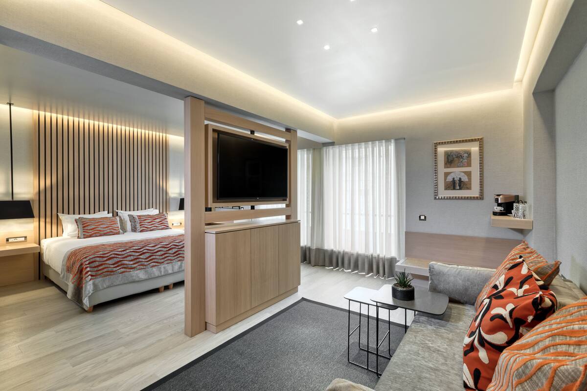 A modern hotel room with a bed, a sofa, a TV, and a small table.