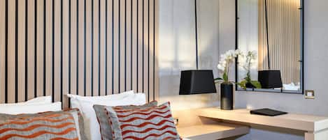 A modern hotel room with a large bed, a desk with a lamp, a mirror, and a vase with flowers.