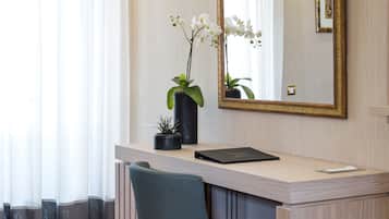 A hotel room with a wooden desk, a chair, a large mirror, and a potted orchid.