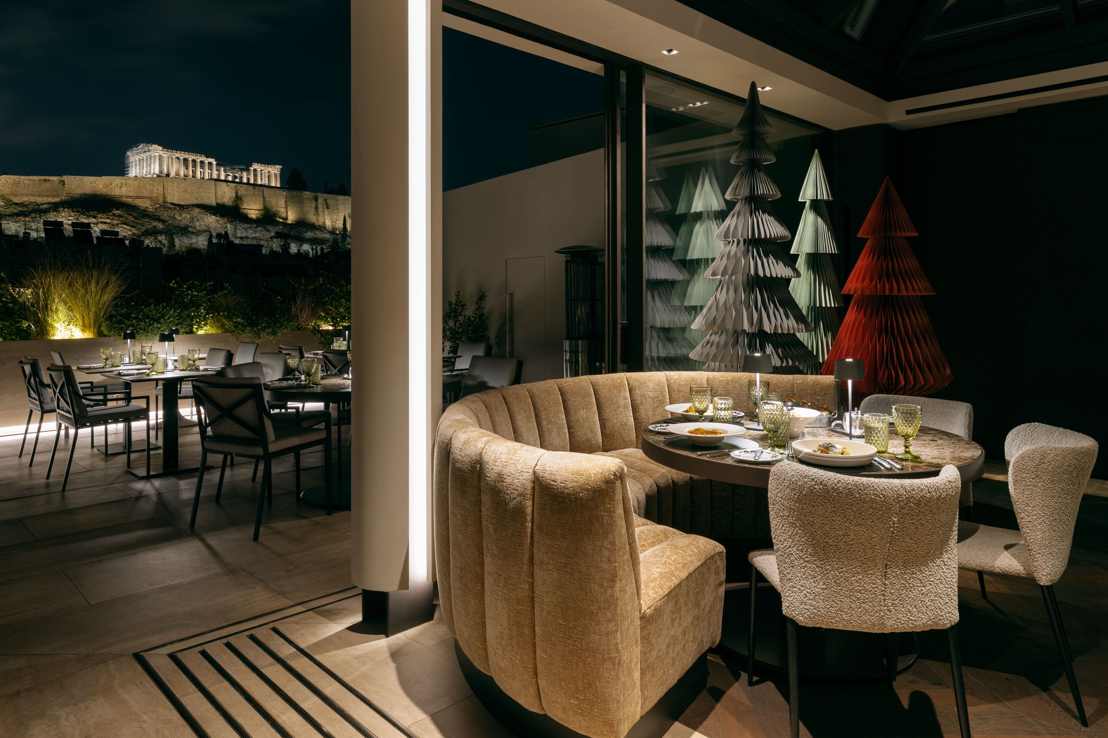 Un comedor moderno con una disposición de asientos curva, vista a un edificio histórico y lámparas de papel con forma de árbol decorativas.