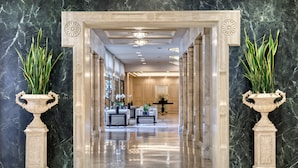 Un elegante ingresso con pareti e pavimenti in marmo, che conduce a una stanza luminosa arredata con mobili e piante.