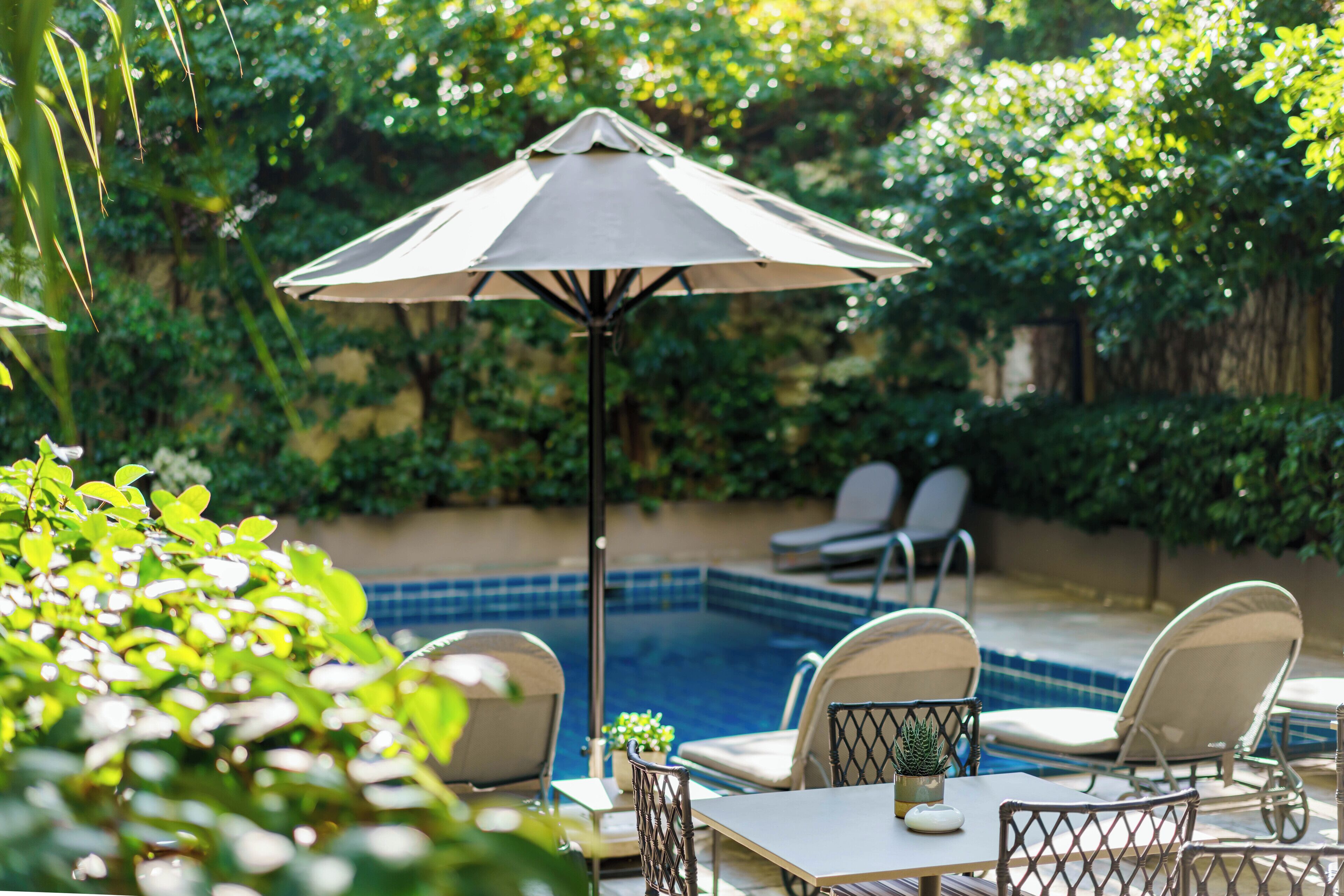 Een zwembadterras met een tafel, stoelen en een parasol.