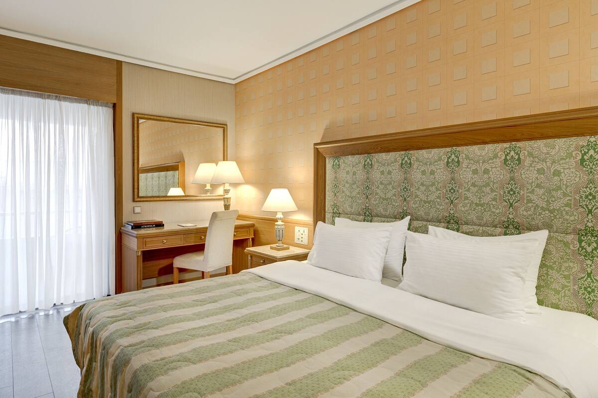 A hotel room with a bed, a desk, a chair, a lamp, and a mirror.