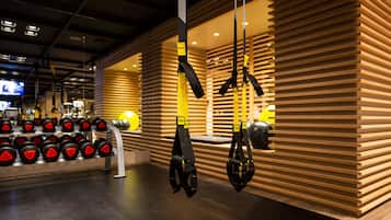 Une salle de sport équipée de matériel de musculation, notamment des haltères et des systèmes d’entraînement en suspension TRX.