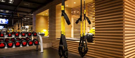 A gym with weightlifting equipment, including dumbbells and TRX suspension trainers.