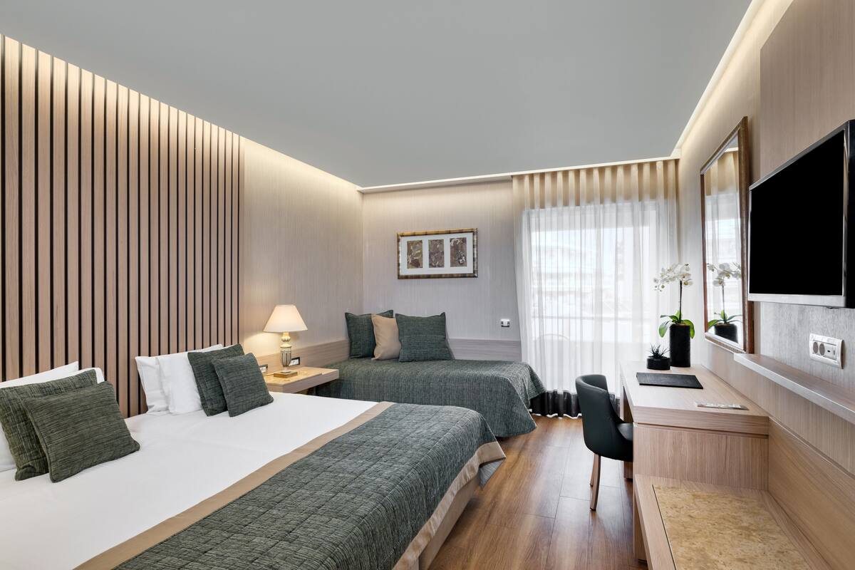 A hotel room with two beds, a desk, a TV, and a window with curtains.