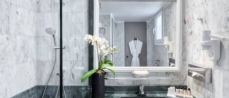 A modern bathroom with a large mirror, a shower, a sink, and a potted orchid.