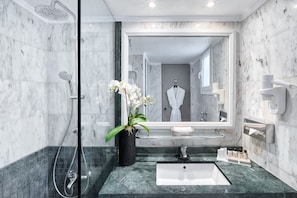 A modern bathroom with a large mirror, a shower, a sink, and a potted orchid.