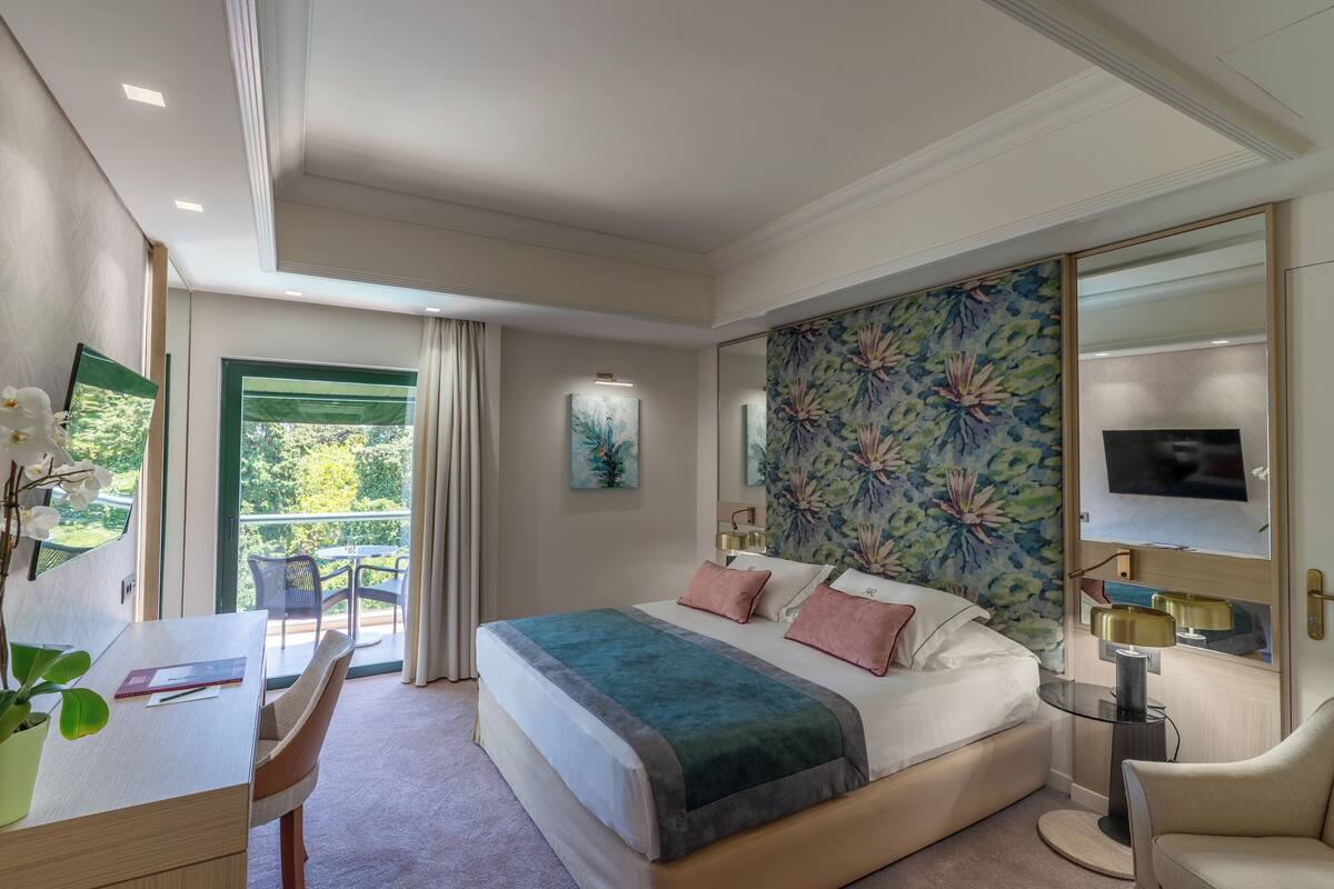A modern hotel room with a large bed, a desk, and a balcony.