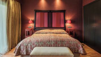 A bedroom with a large bed, two bedside tables, a bench, a wardrobe, and a headboard with built-in lighting.