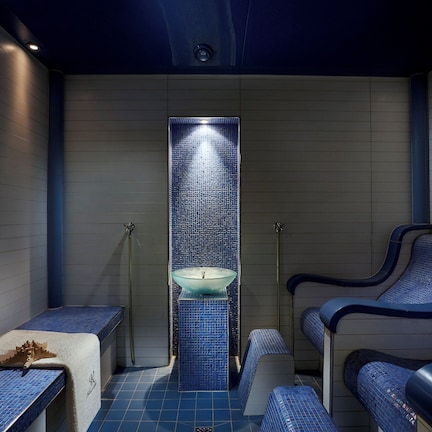 A spa room with a central glass sink, blue tiled benches, and a tiled floor.