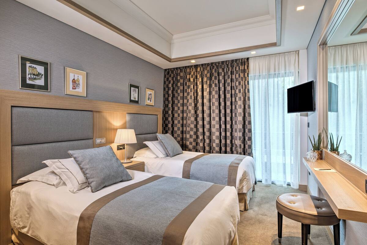 A hotel room with two beds, a desk, and a TV.