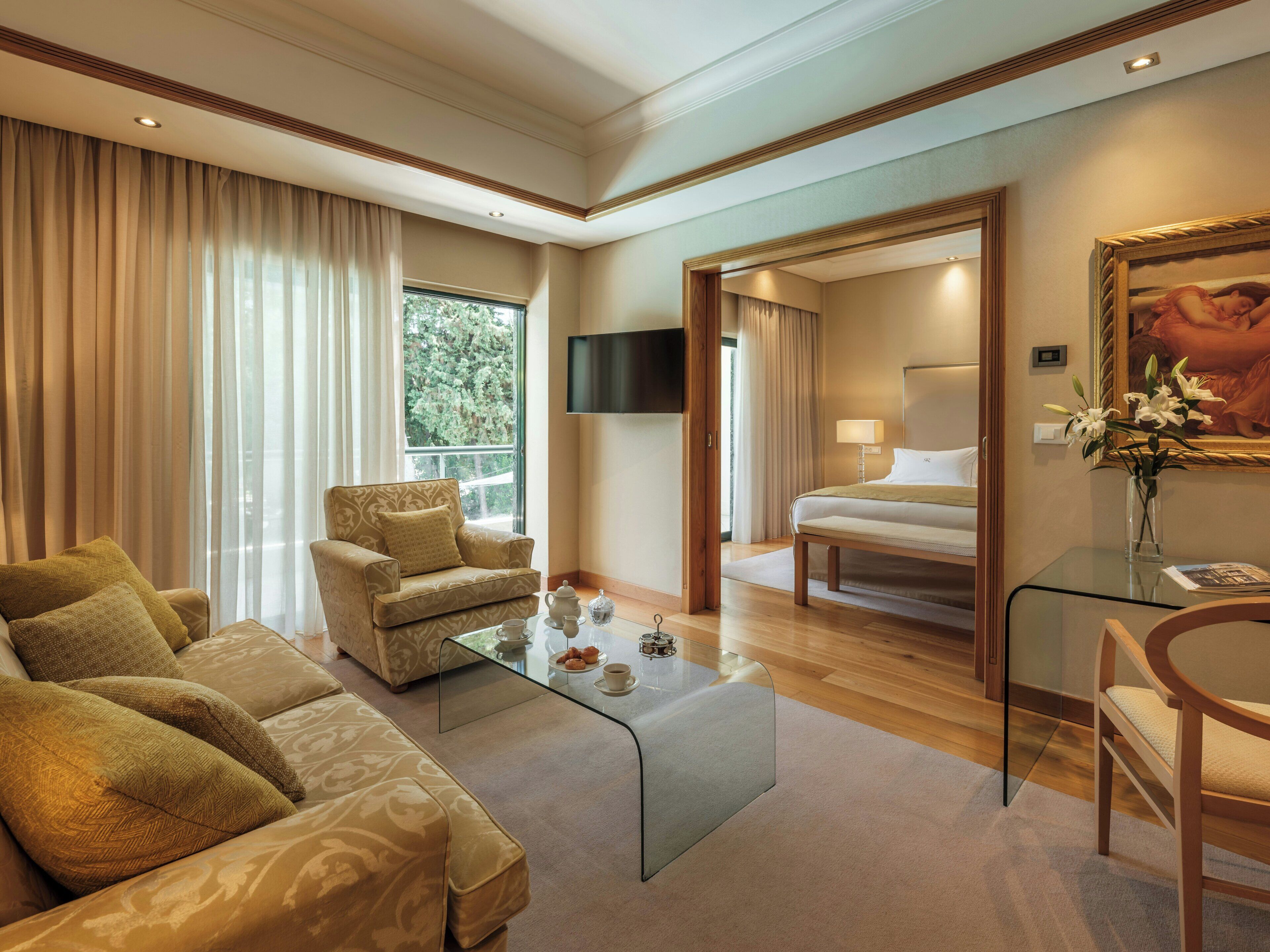 Una habitación de hotel con sofá, una mesita de vidrio, cama, televisor y un cuadro.
