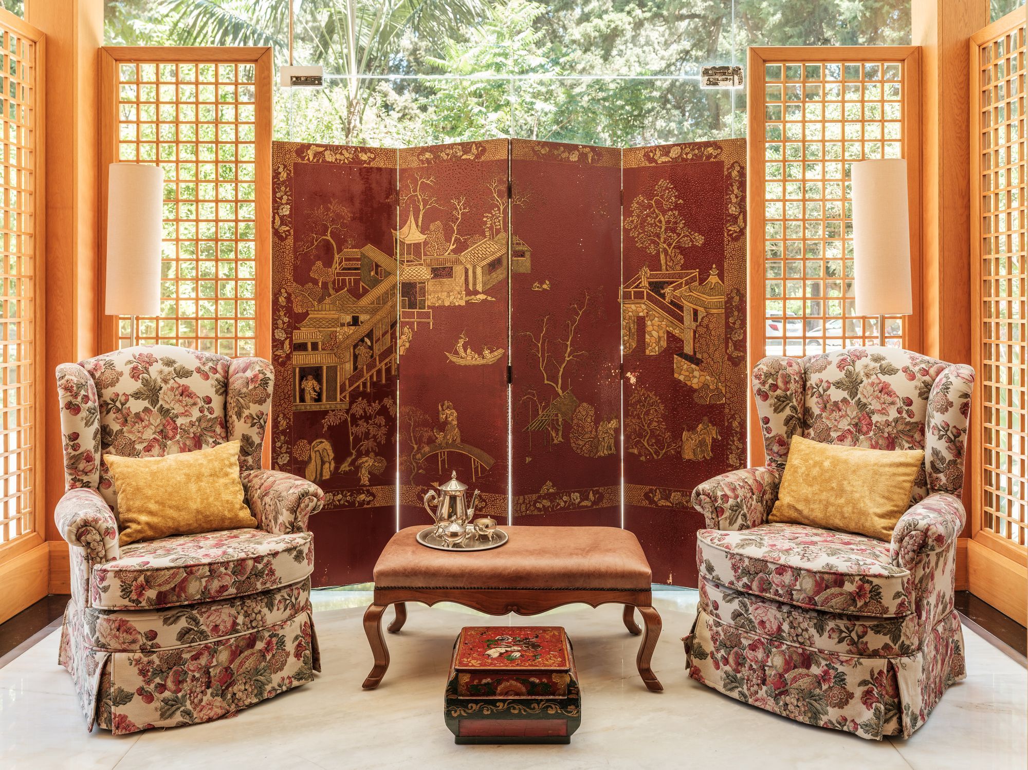 Een klassieke kamer met twee bloemenarmstoelen, een lage tafel en een decoratieve schutting met gedetailleerde versieringen.