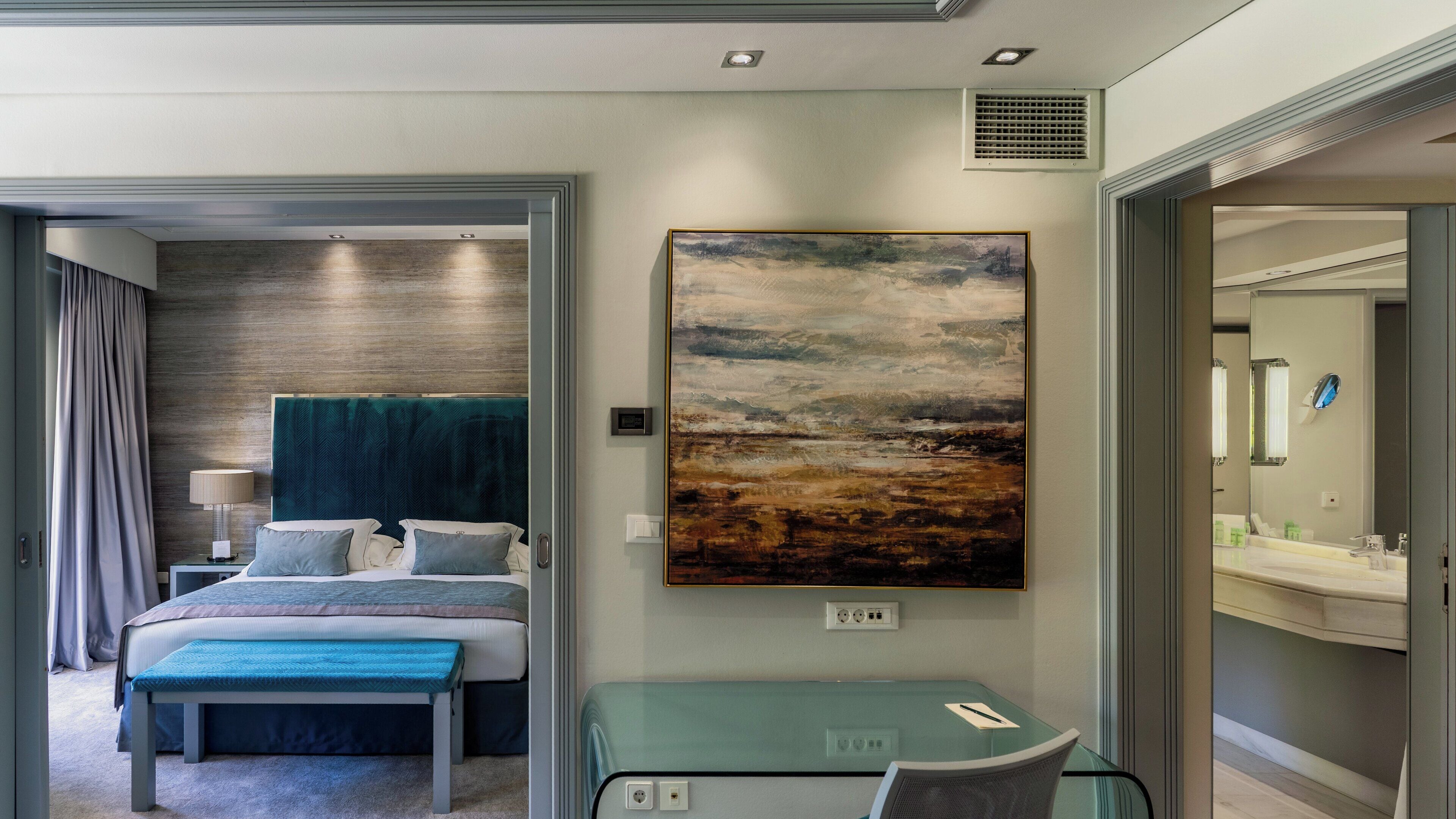 A modern hotel room with a bed, bedside table, lamp, and a large painting on the wall.