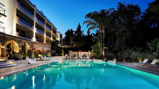 Una piscina con sillones de descanso, una zona de estar cubierta y un edificio con varios balcones.